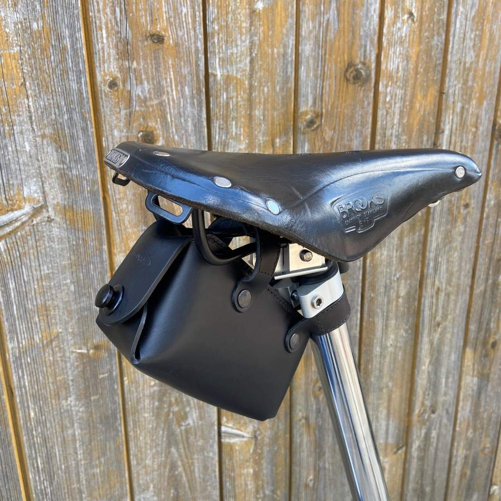 Black bicycle saddle bag with black hardware against a wooden background