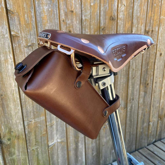 Brown leather saddlebag attached to a bicycle frame against a wooden background