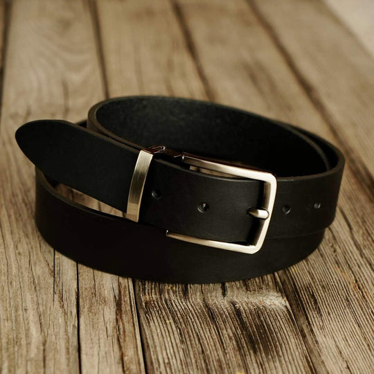 Black leather belt with a buckle on a wooden surface