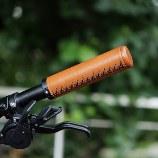 Honey leather bicycle handlebar grip with stitching detail against a blurred green background